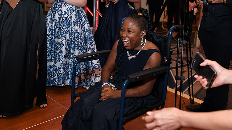 lavishly dressed girl laughing in the prom dance floor while sitting on her wheelchair.